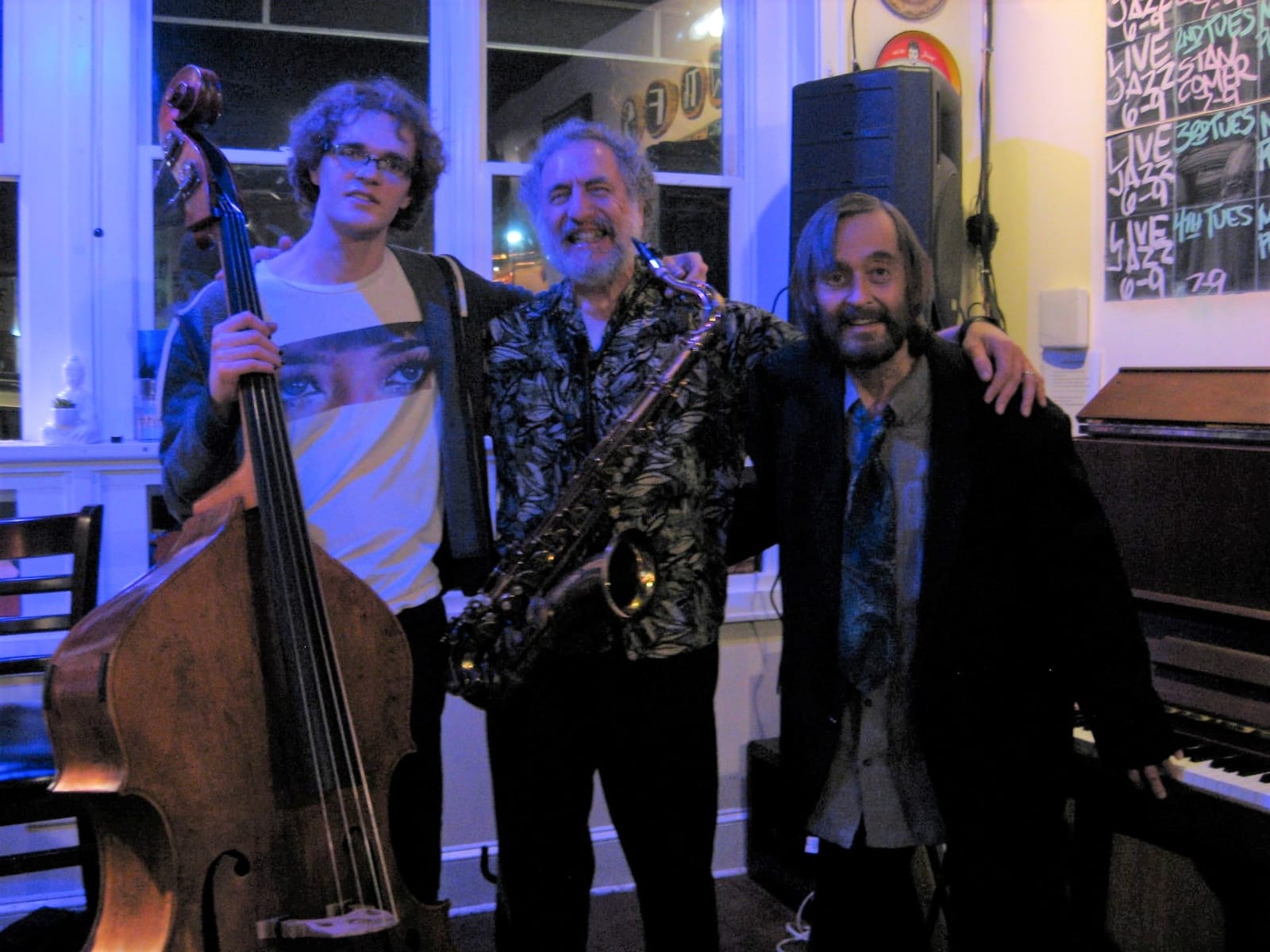 The Jazz Posse standing arm in arm after a set at Rougarou, a bass player holding an upright, David Kreimer with a tenor sax, and Marc Puricelli beside an upright piano.